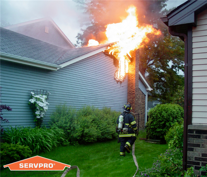 firefighter putting out active house fire. SERVPRO logo in bottom left corner.
